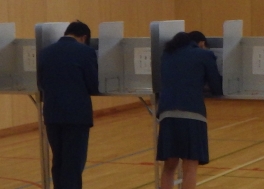投票記載台で投票用紙に記載している様子を後ろから撮影しています。