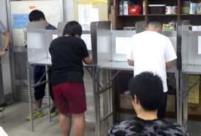 投票記載台で、生徒が投票用紙に記入している様子を後ろから撮影しています