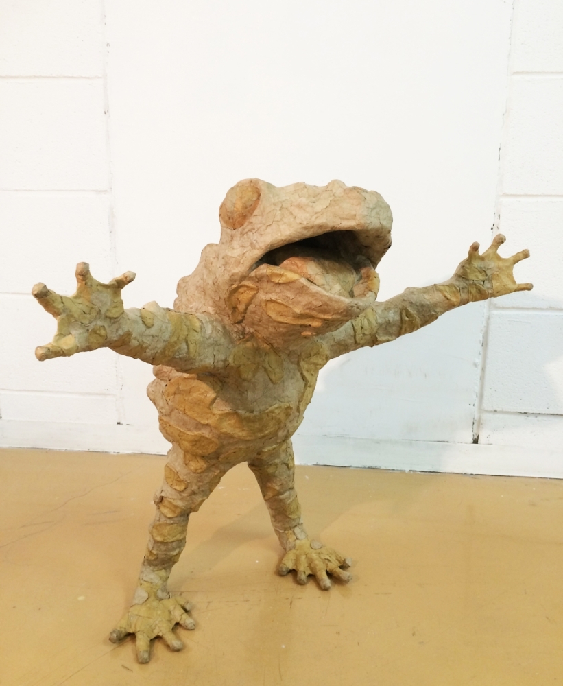 ダンボールでできたカエル、両手を挙げて立っている。
